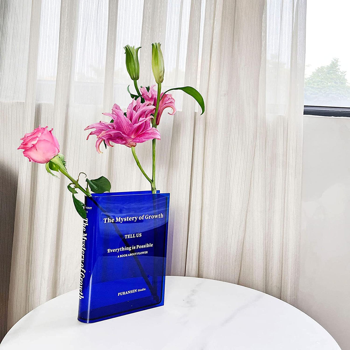 Clear book-shaped flower vase styled on a shelf